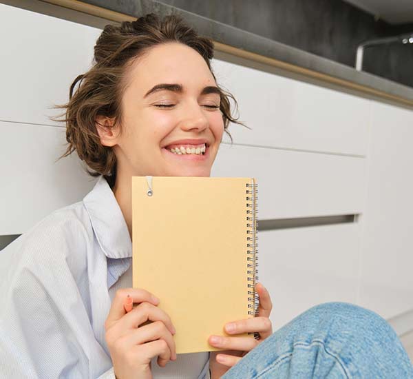 personne souriante et tenant un carnet contre elle